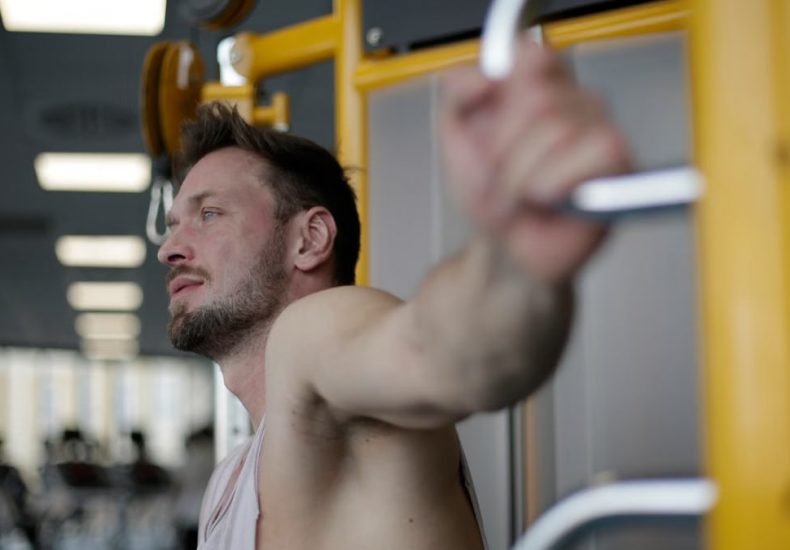 Muscular man exercising on gym equipment, demonstrating strength and focus in a fitness environment.